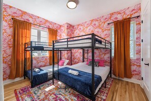Dormitorio con literas, papel tapiz floral, cortinas naranjas y alfombra estampada.