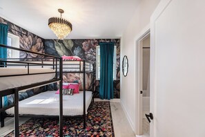 Une chambre avec des lits superposés, un mur décoré d’une fresque florale, un lustre et un tapis à motifs.