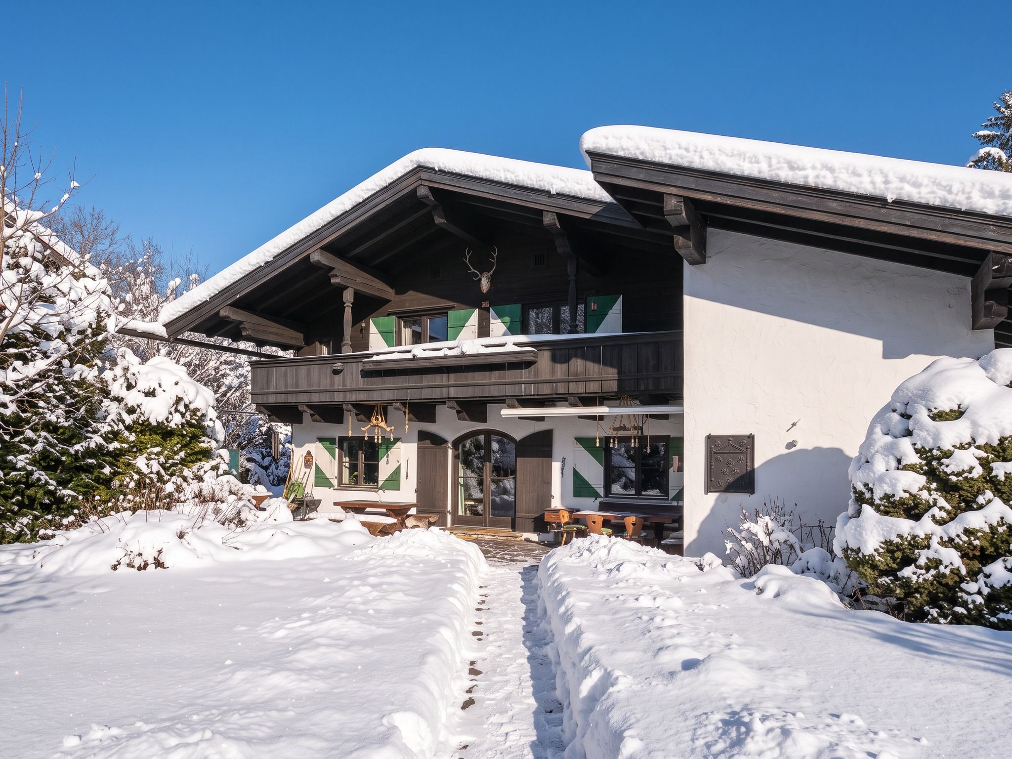 A chalet-style building with a wooden exterior and snow-covered roof, surrounded by snow-covered trees and a clear sky.
