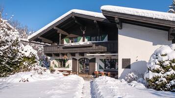 A chalet-style building with a wooden exterior and snow-covered roof, surrounded by snow-covered trees and a clear sky.