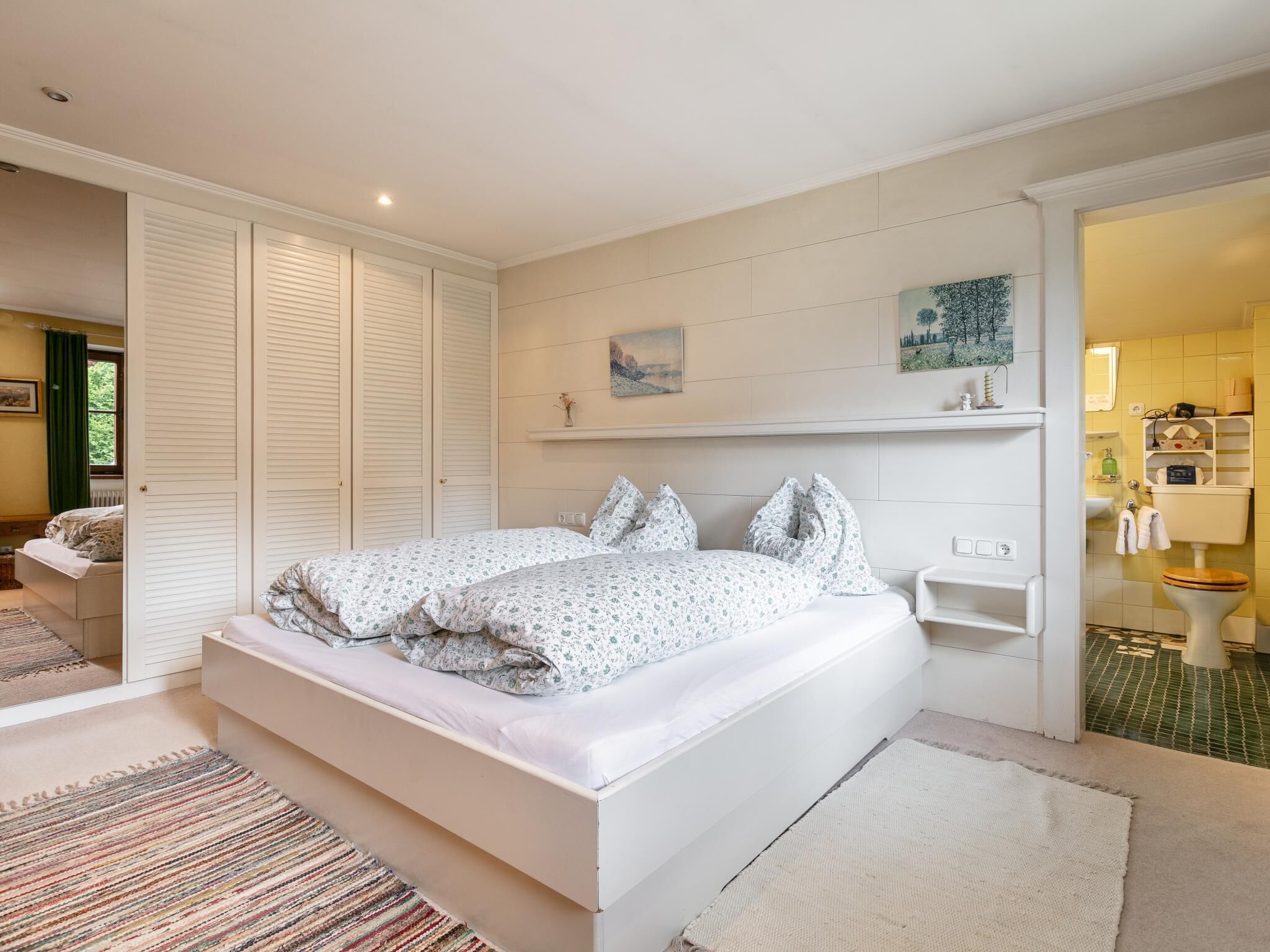 A bedroom with a large bed, a walk-in closet, and a bathroom visible through an open door.