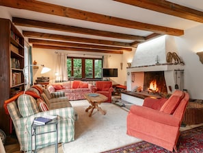 A cozy living room with a fireplace, wooden beams, a television, and a bookshelf. - Apartment, 800m to Hahnenkamm & ski lift (Kitzbühel)
