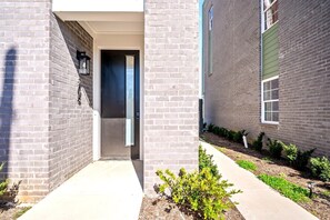 A modern building entrance with a brick facade, a door, and a small garden area with plants. - The Encore - Rooftop Hot Tub/Game Room/Sleeps 12 (Nashville)