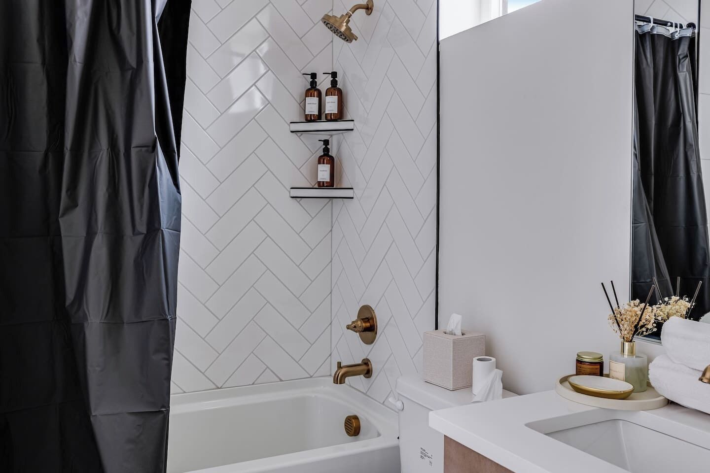 Ein modernes Badezimmer mit weiß gefliestem Rückwand in Fischgrätmuster, einer Badewanne, einem Waschtisch mit Spiegel und einer Dusche mit goldfarbener Armatur.
