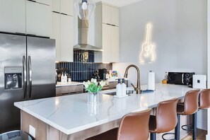 A modern kitchen with a stainless steel refrigerator, a built-in water dispenser, a central island with bar stools, and a neon guitar light.