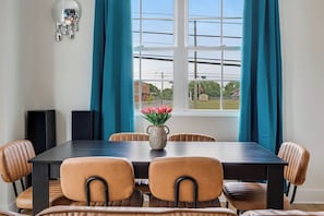 A dining room with a dark wooden table, six brown chairs, a vase with pink flowers, and teal curtains. - The Main Stage - Rooftop Hot Tub/Game Room/Groups (Nashville)