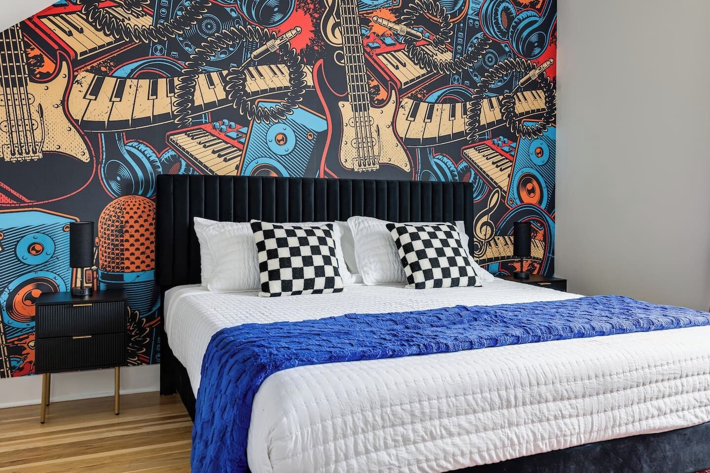 Een slaapkamer met een bed, geruit kussens, een blauwe deken en een muur met een muurschildering over muziek.