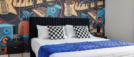 Un dormitorio con cama, almohadas de estampado vichy, manta azul y pared con un mural de temática musical.