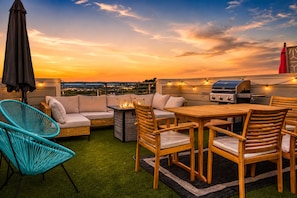A rooftop patio with a grill, seating area, and a view of the cityscape at sunset. - The Main Stage - Rooftop Hot Tub/Game Room/Groups (Nashville)