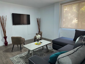 A modern living room with a sofa, armchair, and a coffee table. A flat-screen TV is mounted on the wall. - 2-bedroom apartment in vibrant Ciudad de Mexico Roma Norte (Ciudad de México)