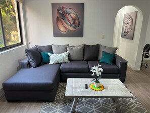 Un salon moderne avec un canapé d’angle, une table basse et deux tableaux abstraits.