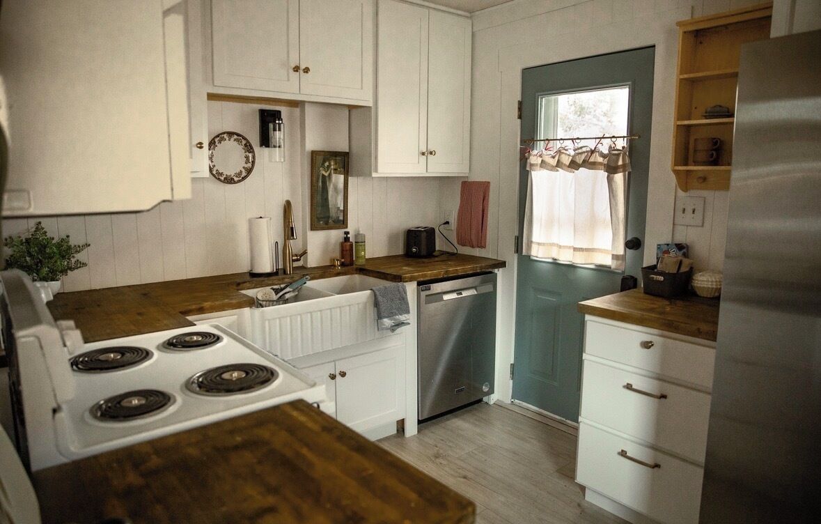 A kitchen with white cabinets, a wooden countertop, a dishwasher, and a stainless steel refrigerator.