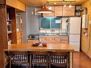 A compact kitchen with a wooden table, four chairs, a stove, a sink, and a refrigerator.