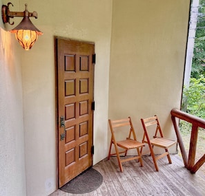 A wooden door with a metal handle, two wooden chairs, and a porch with a wooden railing.