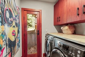 A laundry area with a washing machine, a wooden cabinet, and a colorful abstract painting on the wall. - Private Wooded Breck Retreat - Sauna, Wet Bar & Mtn Views (Breckenridge)