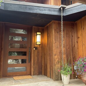A wooden exterior with a door, a wall-mounted light fixture, and a hanging planter with flowers. - Private Wooded Breck Retreat - Sauna, Wet Bar & Mtn Views (Breckenridge)