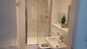 Une salle de bain moderne avec une douche à parois de verre, un lavabo blanc et un petit marchepied menant à la douche.