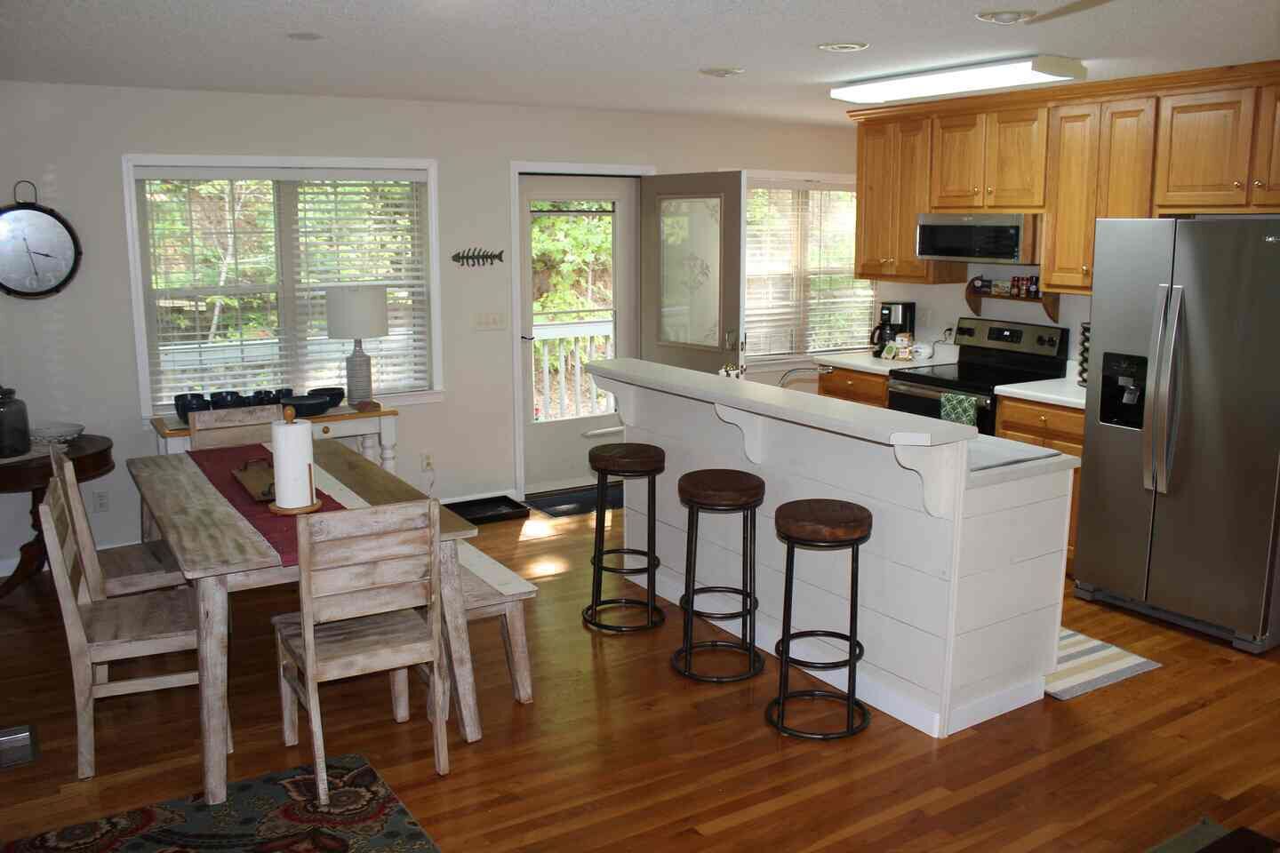 A kitchen with wooden cabinets, a stainless steel refrigerator, a bar stool area, and a dining table with chairs.