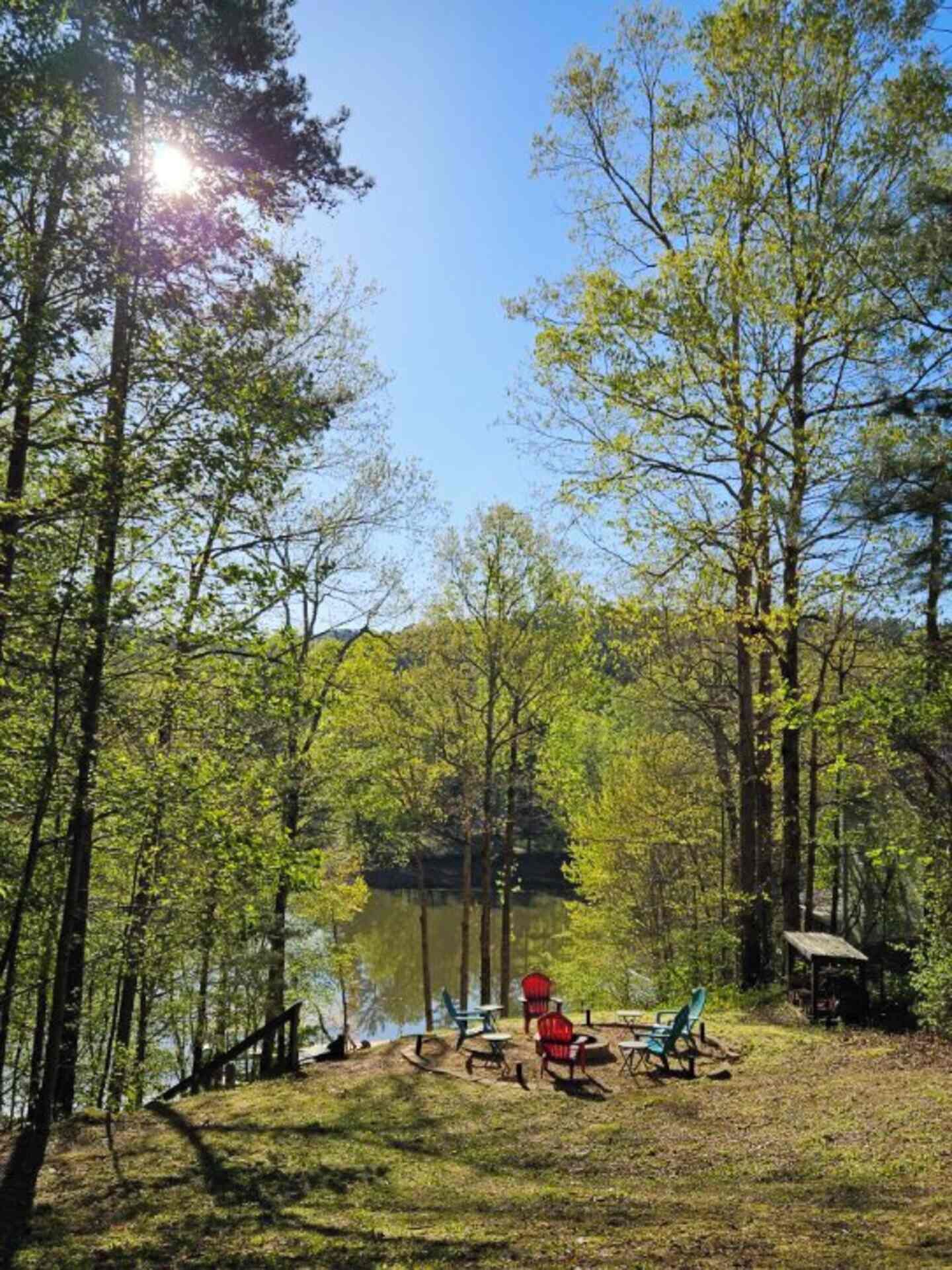 A lakeside campsite with picnic tables and chairs, surrounded by tall trees and a clear sky.