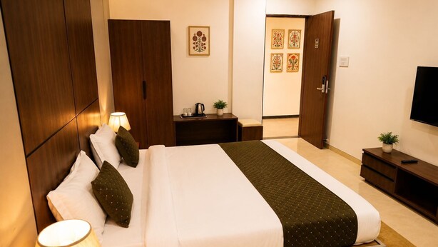 A hotel room with a bed, bedside lamps, a nightstand, a TV, and a door leading to another room.