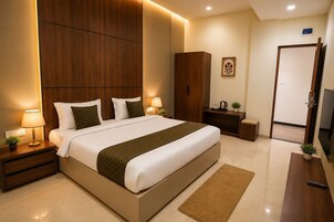 Un dormitorio de hotel moderno con una cama grande, lámparas de noche, un armario de madera, una mesita con una planta y un televisor.