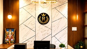A reception desk with a marble countertop, a logo with a crown and the letter 'R', and a modern chandelier.