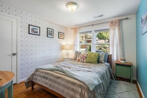 A bedroom with a bed, a nightstand, a window with curtains, and a door. - Magnolia Oasis (Seattle)