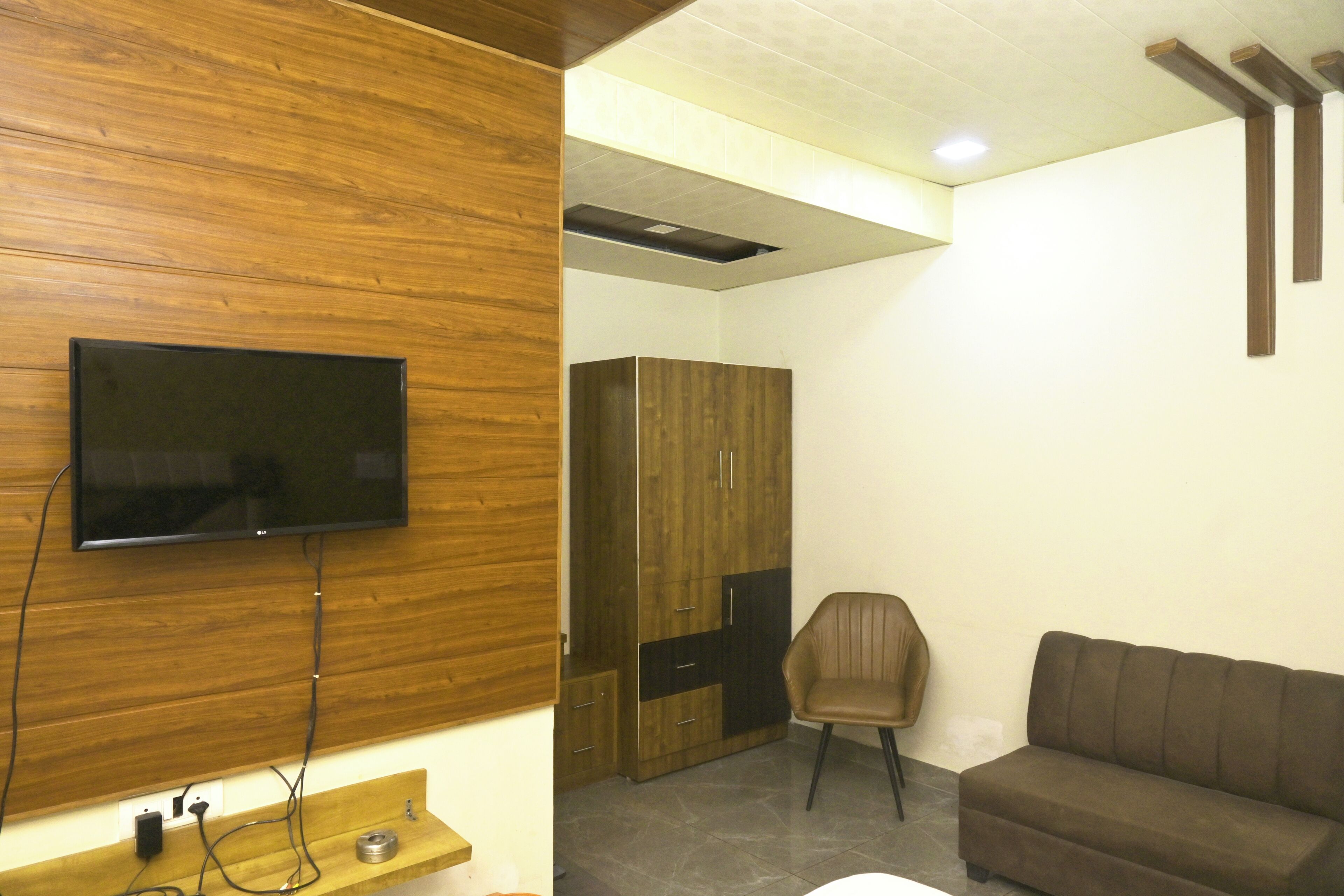Habitación con televisión de pantalla plana montada en una pared de madera, un armario, un sillón de cuero marrón y un sofá marrón.