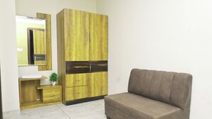 A room with a brown sofa, a wooden wardrobe with two drawers, a small bedside table with a plant, and a mirror on the wall.