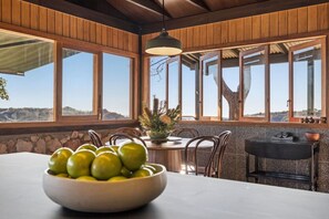 A dining area with a table, chairs, a bowl of fruit, and a view of the outdoors.