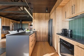 A modern kitchen with wooden cabinetry, a central island, and a built-in oven. - Lakeview Farm @ Maleny (North Maleny)