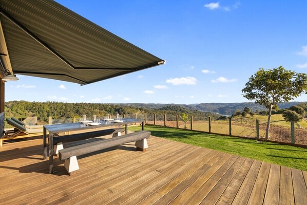 An outdoor deck with a table and benches, overlooking a grassy area and distant hills.