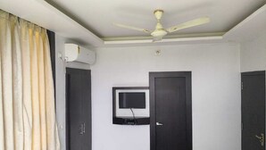 A room with a ceiling fan, a mounted television, and two doors.