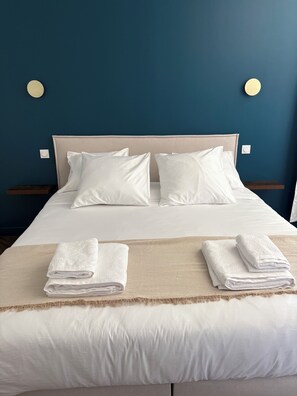 A neatly made bed with white linens and pillows, a beige throw blanket, and two folded towels on a wooden nightstand. - Maison de Garrigue Estanh – A charming estate with a pool near Narbonne (Bages)