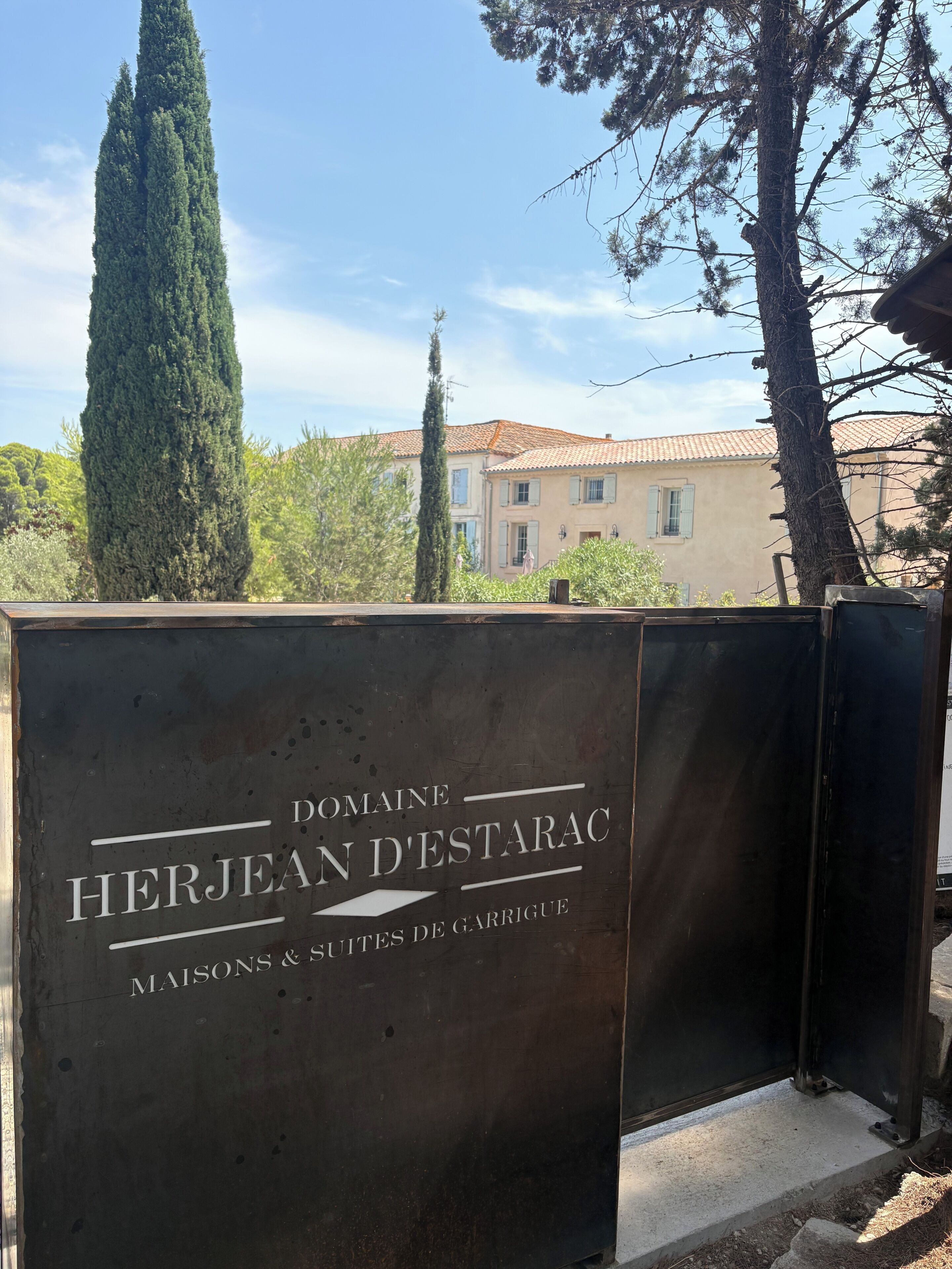 A sign for Domaine Herjean D'Estarac with the text 'MAISONS & SITES DE GARRIGUE' indicating a property with houses and sites.