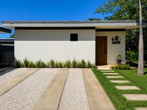 A modern house with a concrete pathway leading to the entrance, a small garden with various plants, and a wooden door. - Dream House 20 Min from Tamarindo Beach (Guanacaste)