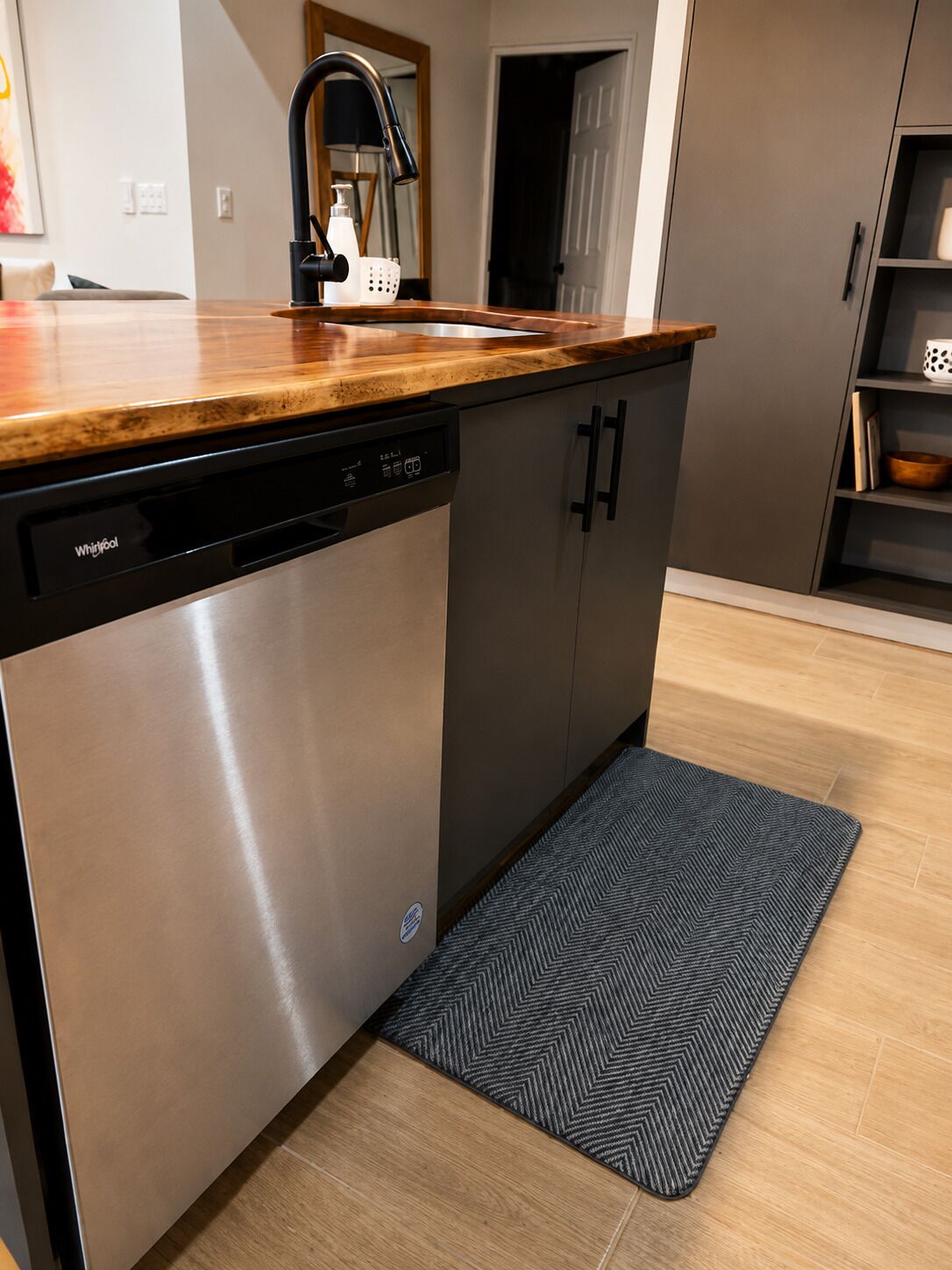 Une cuisine moderne équipée d’un lave-vaisselle, dotée d’un plan de travail en bois et agrémentée d’un tapis à motifs en chevrons.