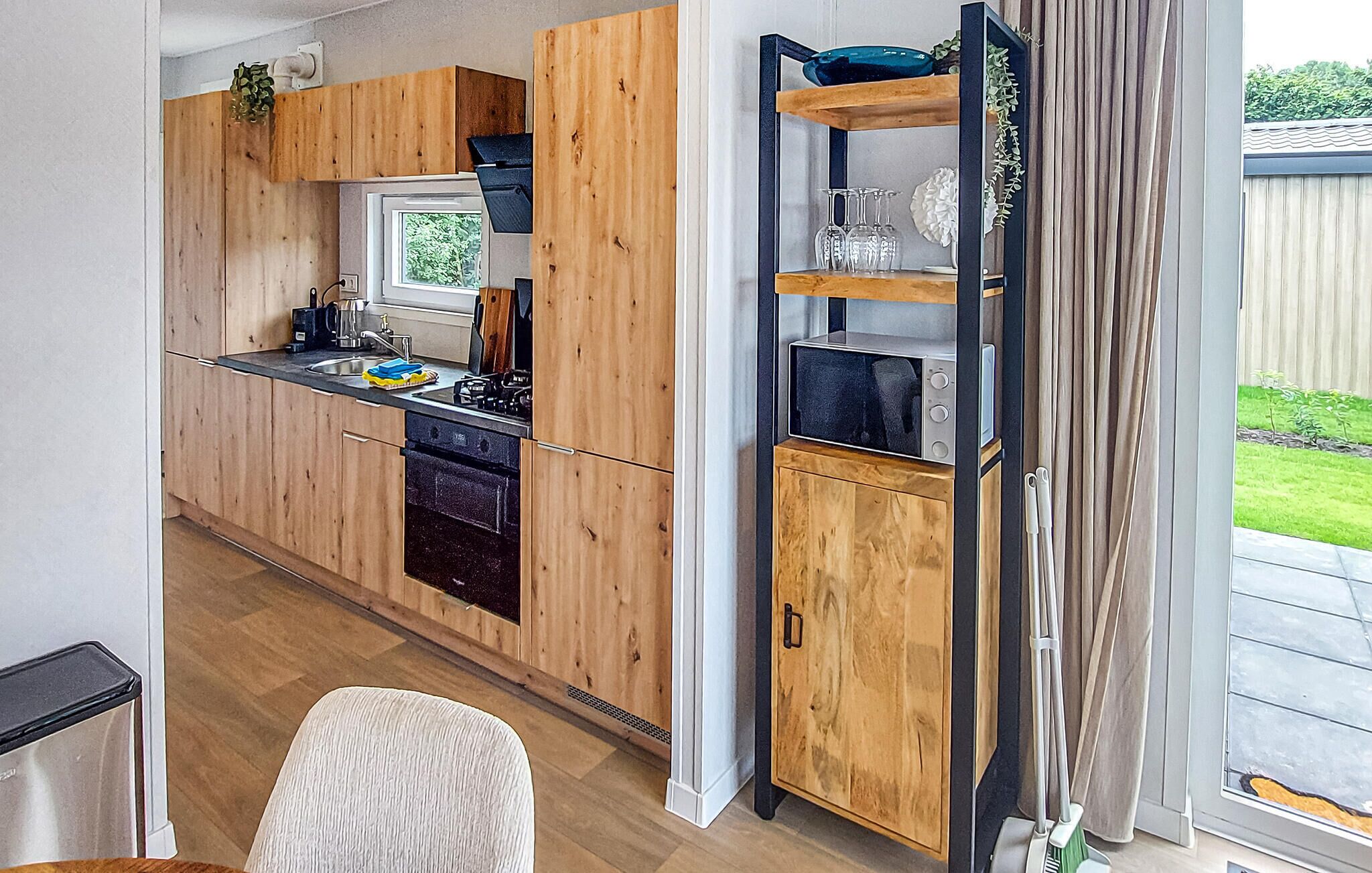 Une cuisine moderne avec des meubles de rangement en bois, un four encastré et une fenêtre donnant sur un jardin.