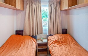 Ein schmaler Raum mit zwei Betten, einem Fenster mit Vorhängen und einer Heizung.