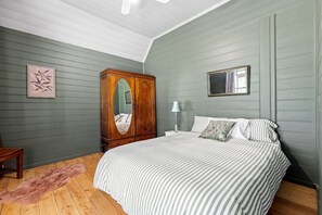 A bedroom with a bed, a wooden wardrobe, a mirror, and a rug.