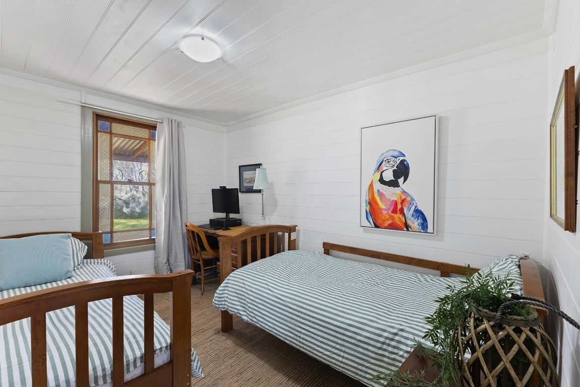 A room with two single beds, a desk with a chair, a computer, and a framed artwork on the wall.