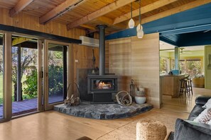 A cozy living room with a stone fireplace, wooden beams, and a view of the outdoors.
