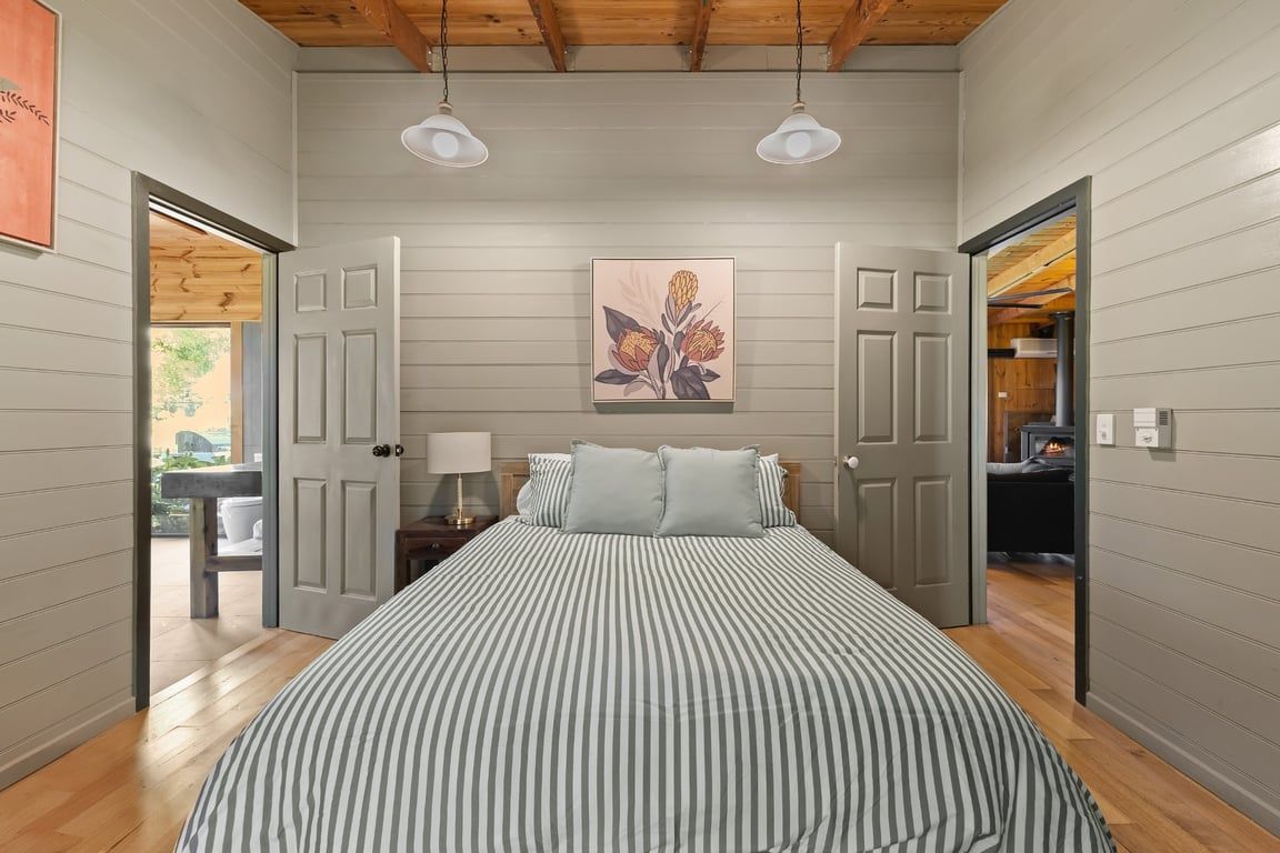 Een slaapkamer met een bed, twee bedlampen, een schilderij aan de muur en een deur die naar een andere kamer leidt.