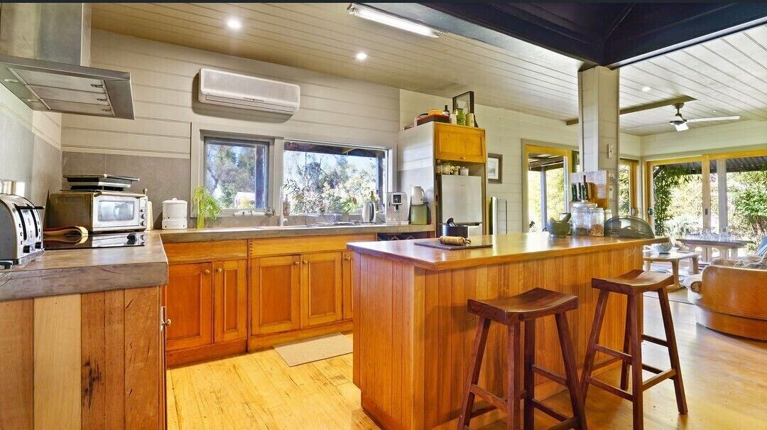 A modern kitchen with wooden cabinets, a central island with stools, and a view of the outdoors.