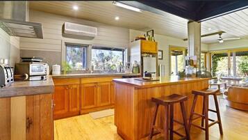 A modern kitchen with wooden cabinets, a central island with stools, and a view of the outdoors.
