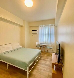 Ein Hotelzimmer mit einem Bett, einem kleinen Tisch mit Stühlen, einer Klimaanlage und einem Fernseher auf einem Holzboden.