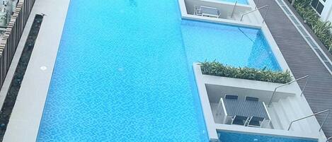 A rectangular swimming pool with a tiled deck and a small deck area with a chair.