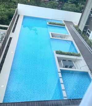 Uma piscina retangular com um deck ladrilhado e uma pequena área de deck com uma cadeira.
