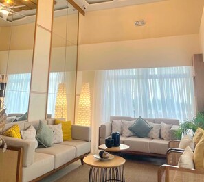 Ein modernes Wohnzimmer mit einer Couch, einem Couchtisch und einem großen Fenster mit durchsichtigen Vorhängen.