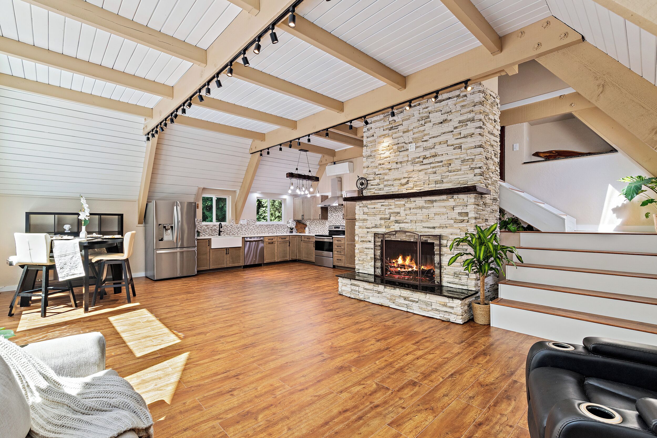 A spacious living area with a stone fireplace, wooden beams, and a kitchen in the background.